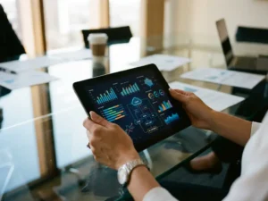 Businesswoman holding tablet displaying colorful data analytics charts at modern conference table with natural lighting.
